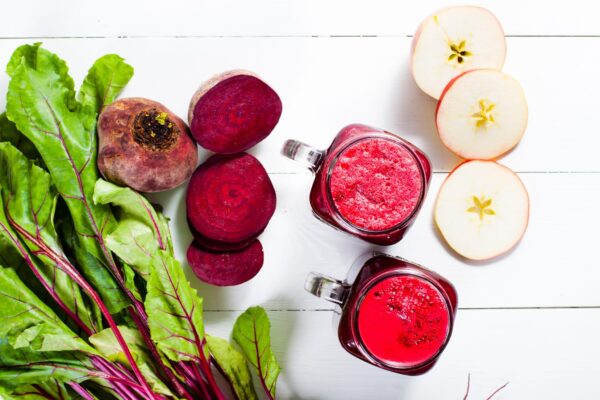 Cura Detoxifiere Red smoothies from beetroot, beet leaves and apple on white wooden table. Flat lay.