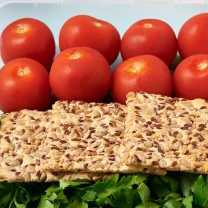 Înapoi la școală: ce pui în ghiozdanul copilului în loc de croissant 1 Cutie de prânz cu compartimente, cu roșii cherry, pâine crocantă integrală și țelină, pe fundal albastru