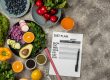 O fișă de plan alimentar și un centimetru de croitorie, înconjurate de legume, fructe de pădure și avocado