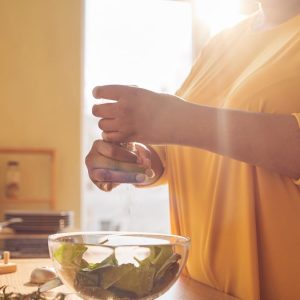 Postul intermitent 16:8: cui i se potrivește, cui nu, și cum îl începi corect 1 Persoană care condimentează un bol cu salată în bucătărie, în lumina ferestrei