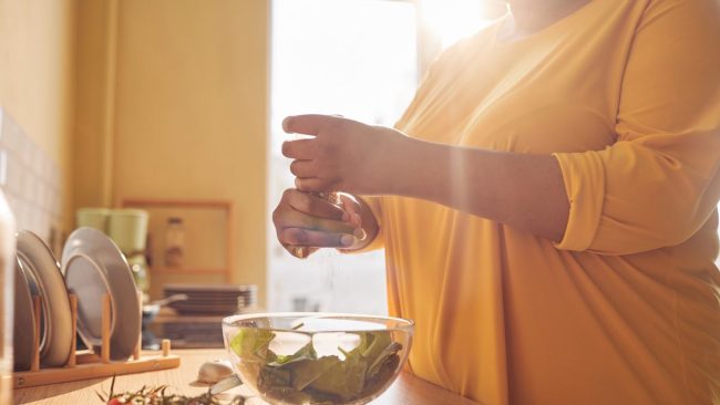 Persoană care condimentează un bol cu salată în bucătărie, în lumina ferestrei