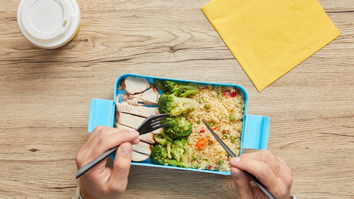 Pachet de prânz la birou: 12 combinații care nu se strică și nu te lasă flămând la 16:00 1 Pachet de prânz la birou: cutie cu pui, broccoli și cuscus, pe un birou de lemn, lângă o cafea
